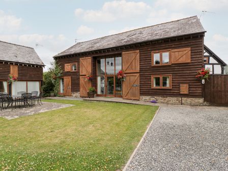 A wooden barn style building with large glass doors flowers and outdoor seating at Tippets View in Luntley near Pembridge