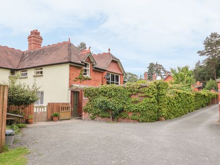 A brick house with a tiled roof and an ivy-covered fence along a driveway at Riverside Cottage in Llanwrthwl near Rhayader