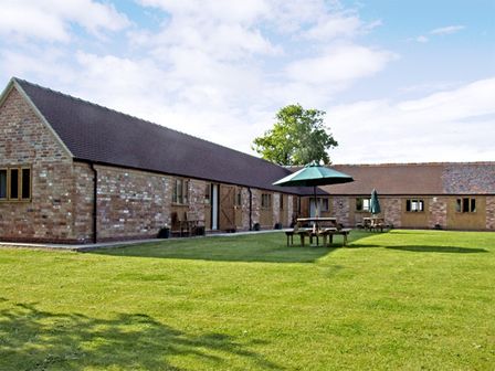 A brick building with a tiled roof and wooden doors and windows next to a lawn with picnic tables and umbrellas at The Dairy in Clifford Chambers near Stratford-upon-Avon