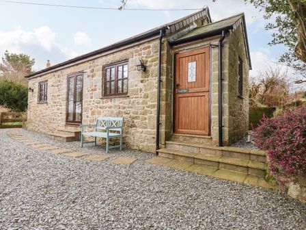 A stone exterior cottage with wooden door and windows a blue bench and gravel yard at Brocks Barn Sweetshouse near Lostwithiel