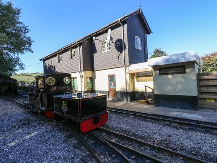 A small black and red train on tracks next to a two-story building with brown siding at The Station Flat in St Newlyn East near Newquay
