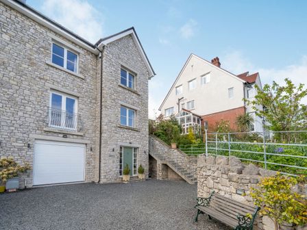 Exterior view of a stone house with a white garage door a staircase leading up to a garden and bench at Hillberry in Grange-Over-Sands