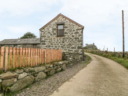 A stone house with a wooden fence and a gravel driveway at Y Stabal in Criccieth
