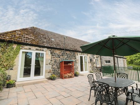A stone patio with black metal table and chairs under a green umbrella at Gardener's Cottage in Belford near Bamburgh