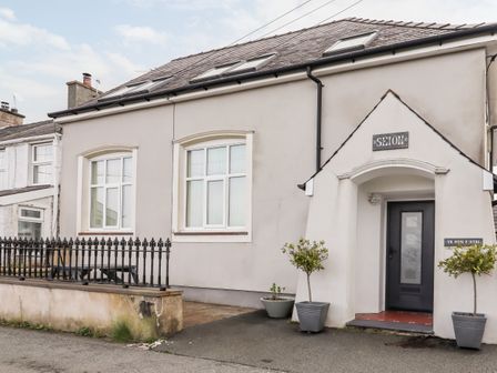 The exterior of a house with white walls two windows two potted plants black metal fence and a black front door at Yr Hen Festri in Y Felinheli