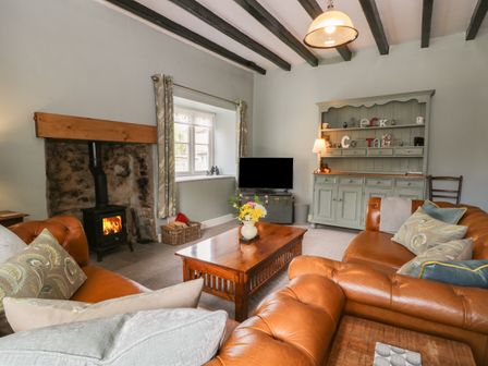A living room with leather sofas a wooden coffee table a wood burning stove and a cabinet at Beck Cottage in Pickering