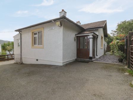 An exterior view of a white cottage with a paved driveway and wooden entrance door at Bangor Cottage in Bangor