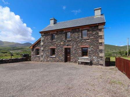 A stone house with six windows and a door in front of a gravel yard at Brandon Holiday Home in Cloghane County Kerry