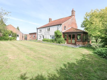 A brick and white house with a conservatory and an adjoining building on a lawn at Lyons Green in Little Fransham near Swaffham