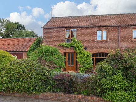 A brick house with a tiled roof surrounded by shrubs and trees at 1 Woods Garth in Wetwang near Driffield