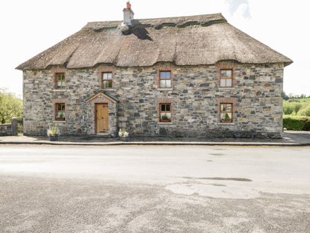 A stone cottage with a thatched roof and six windows by a road at An Maide Ban in Maudabawn near Cootehill County Cavan