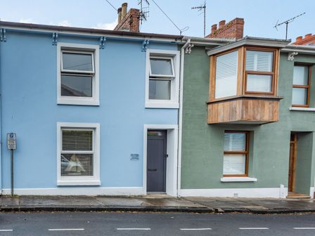 Blue and green terraced houses with windows and doors facing a street with a parking sign at Barafundle House in Tenby