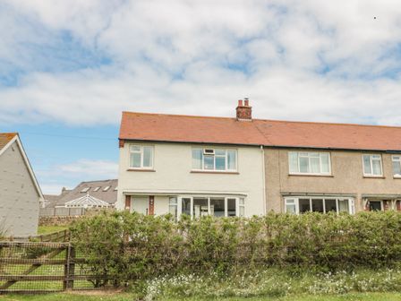 An exterior view of a semi detached house with a hedge and a wooden gate in front at Dune View in Beadnell