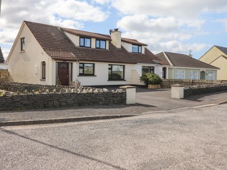 A semi detached house with a brown tiled roof and white exterior walls with a stone wall and driveway at Sea Park Cottage in Lahinch County Clare