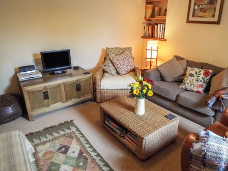 A living room with a television on a wooden cabinet a wicker chair a gray sofa and a wicker coffee table with flowers at Lothlorien Cottage in Cwmgors near Ammanford