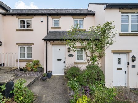 The exterior of a cottage with two white doors numbered 7 and 8 and surrounding plants at Amber Cottage in Cark in Cartmel