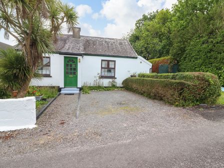 A small white house with a green door surrounded by trees and bushes at Brendan's Cottage in Valentia Island County Kerry
