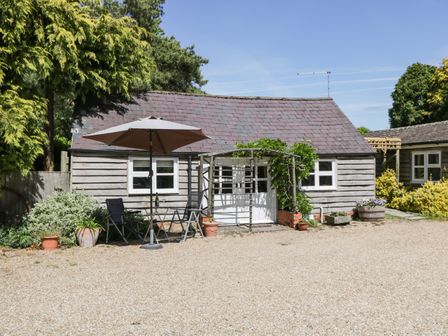 A small wooden building with a slate roof patio umbrella chairs and potted plants outside at The Pottery in Urchfont near Devizes