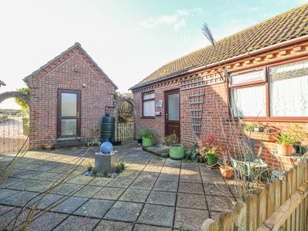 A paved courtyard with potted plants and garden furniture between brick buildings at Robyn's Nest in Brinton near Holt