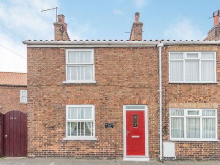 Brick house with two white framed windows and a red front door at Fisher Cottage in Hornsea