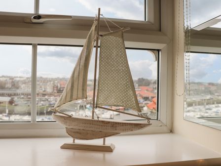 A wooden model sailboat with two fabric sails on a windowsill overlooking a harbor at Cairns Cottage in Whitby
