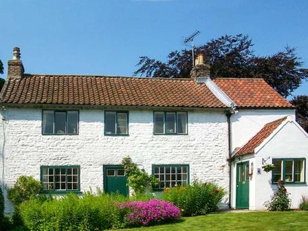 A white cottage with green doors and window frames surrounded by bushes and flowers at The White Cottage in Bridlington