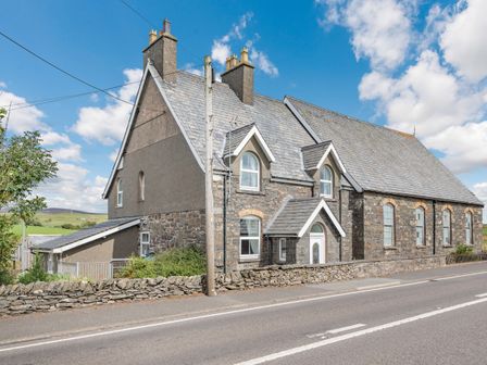 A stone and brick house with multiple chimneys and arched windows by a road at Glan Nug in Rhydlydan near Betws-y-Coed