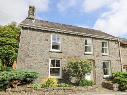 A stone house with four windows a door and plants in front at Derwen Villa in Mydroilyn near New Quay