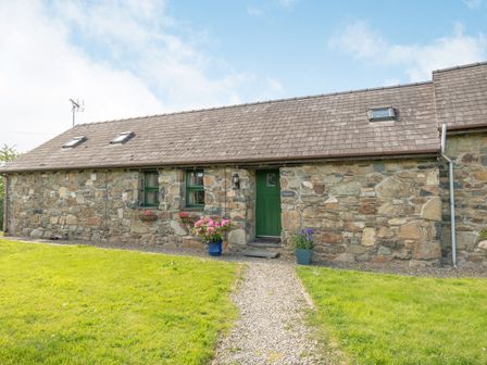 A stone cottage with a green door and windows with flower pots by the entrance at Foxglove in Newport Pembrokeshire