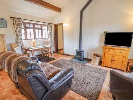 A living room with a leather sofa a wood stove a wooden cabinet with a television and a small dining table at Dairy Barn in Pershore