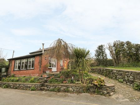 A brick house with multiple windows and a small garden with plants and a paved pathway at Beck Cottage in Pennington near Ulverston