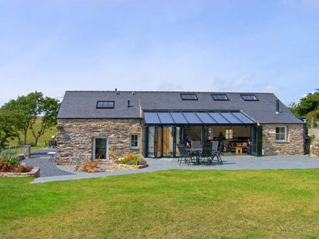 A stone house with multiple skylights and a patio with chairs and tables in a grassy yard at Garth Morthin The Barn in Porthmadog