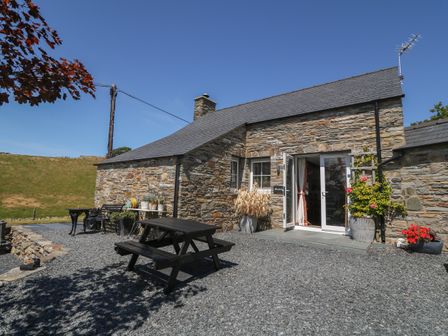 An outdoor patio area with a wooden picnic table and stone house at Garth Morthin The Stables in Porthmadog