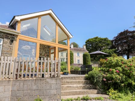 An outdoor patio area with stone steps wooden fence glass extension and garden furniture at Llety'r Wennol Ffarmers near Lampeter