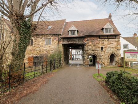A stone and brick archway building with a tiled roof over a paved path at Porter's Lodge in Polesworth