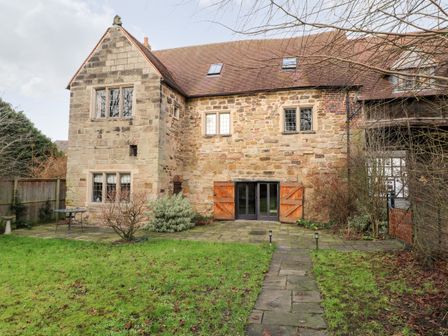 A stone house with a pitched roof and small windows with a garden in front at Gatehouse Croft in Polesworth