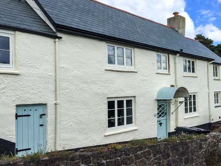 A white plastered house with blue doors and multiple windows behind a stone wall at Greenslades in Exford near Dulverton
