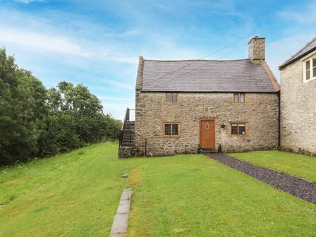 A stone cottage with a slate roof and wooden door surrounded by a grass lawn and trees at Ty Tabitha Wynne Afonwen near Ruthin and Mold