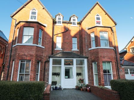 A brick apartment building with a central white door and multiple windows surrounded by plants at Carisbrooke House Apartment 6 Scarborough