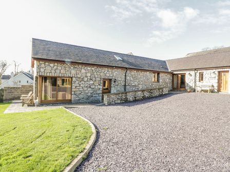 A stone building with a gravel driveway and a grass lawn at Beudy Bach in Llangoed