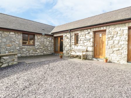 An exterior view of a stone building with a wooden bench and potted plants on a gravel courtyard at Cwt Blawd in Llangoed near Beaumaris