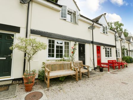 A row of cream-colored cottages with green and red doors and wooden benches outside Wye Valley Cottage Symonds Yat