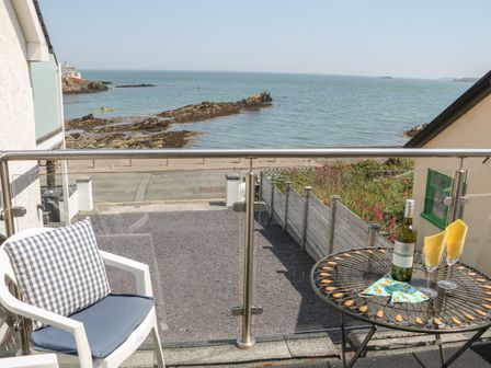 A balcony with a table set with a bottle of wine and two glasses and a chair overlooking the seaside at Min Y Traeth in Bull Bay