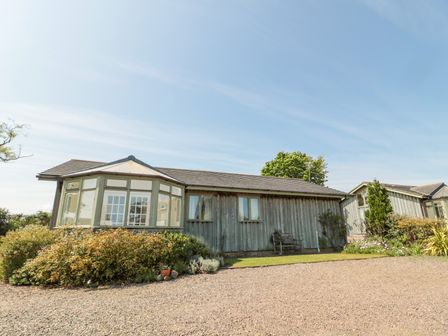 A single-story wooden house with large windows and a garden with shrubs in front at Orchard Lodge in Warkworth