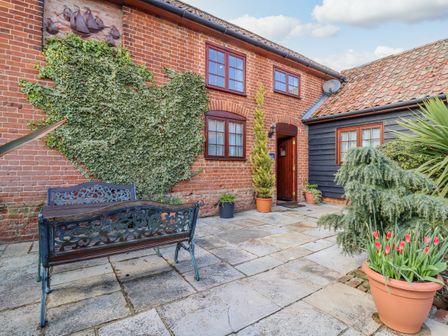 A brick house exterior with ivy on the wall a metal bench and potted plants at Hayloft Cottage in Little Glemham near Wickham Market