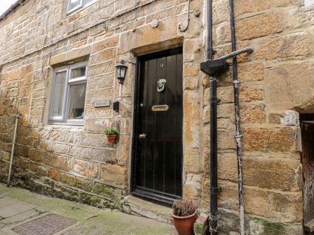 The exterior of a stone building with a black door numbered 9 a window and potted plants at Inglenook Cottage in Whitby