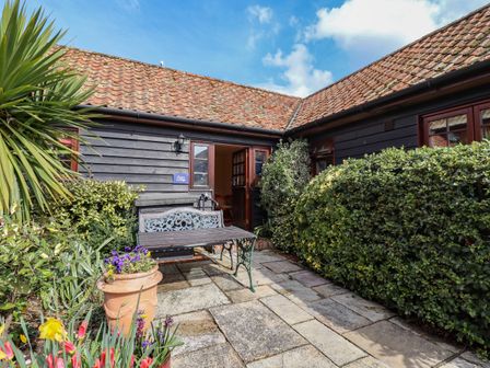 A patio with a bench table potted flowers and hedges outside a cottage at Poppy Cottage in Little Glemham near Wickham Market