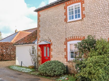 Stone exterior walls of a house with a red door and two white framed windows surrounded by bushes at 28 Oxborough in Oxborough