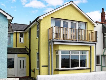 A yellow two-story house with a balcony and large windows at Trysor Y Mor in Borth