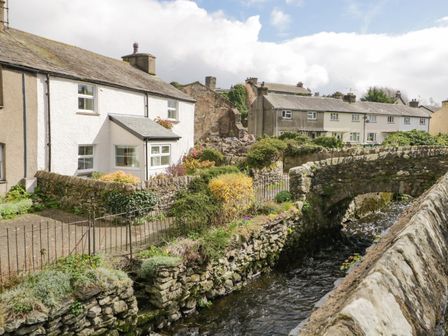 A row of houses by a stone bridge over a flowing stream at 14 Low Row in Cark in Cartmel